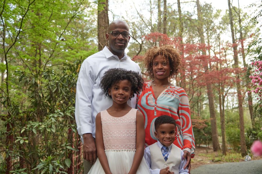 The family of four standing among tall pines.