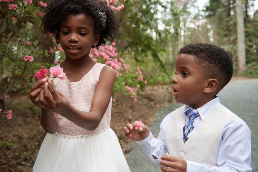 A girl showing a handful of pink blossoms to her brother.