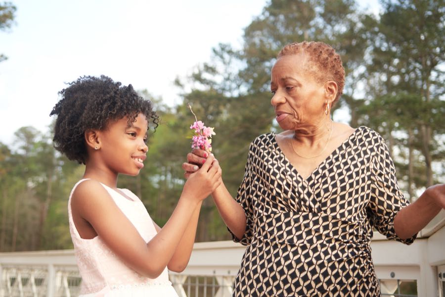 A girl handing a flower to her grandmother.