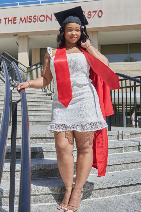 Standing on the campus steps, hand on the rail, in cap and gown.