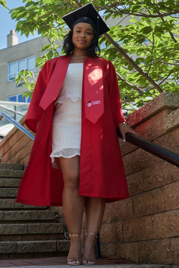 A graduate in cap and gown on the campus steps.
