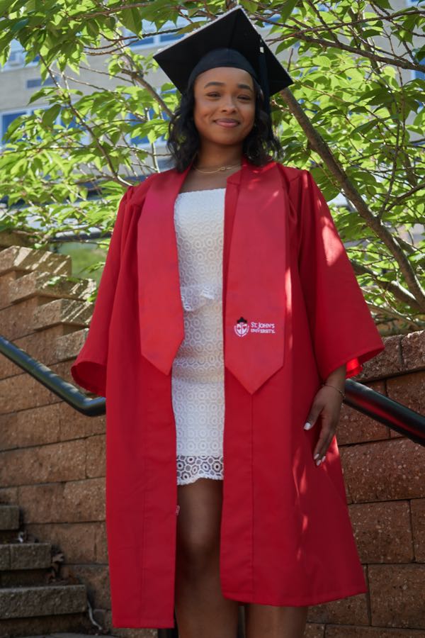 Closer portrait in cap and gown under green trees.