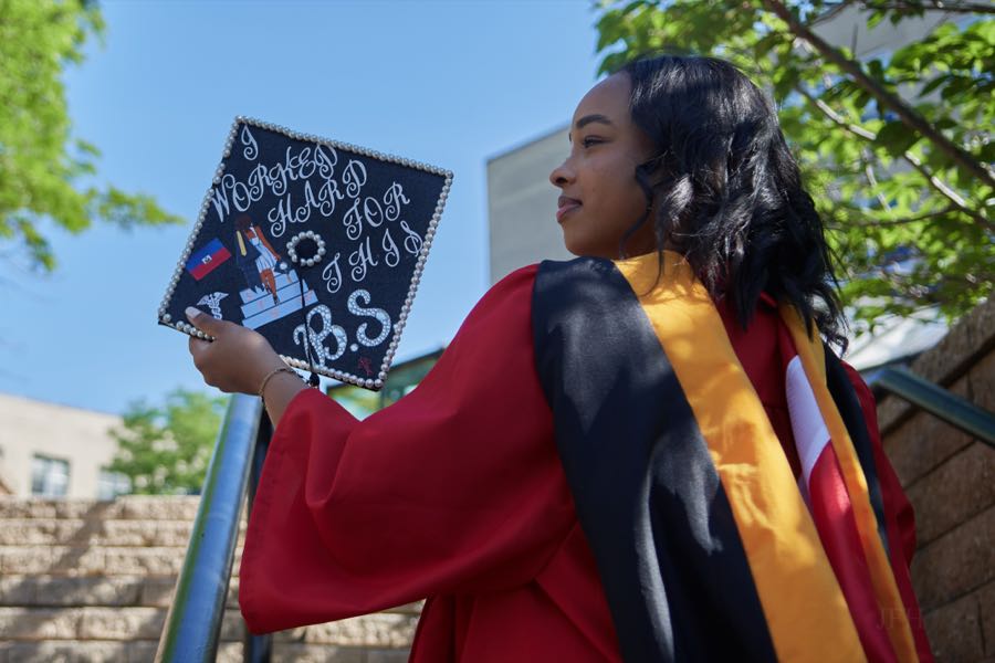 Holding the decorated cap up beside her face.