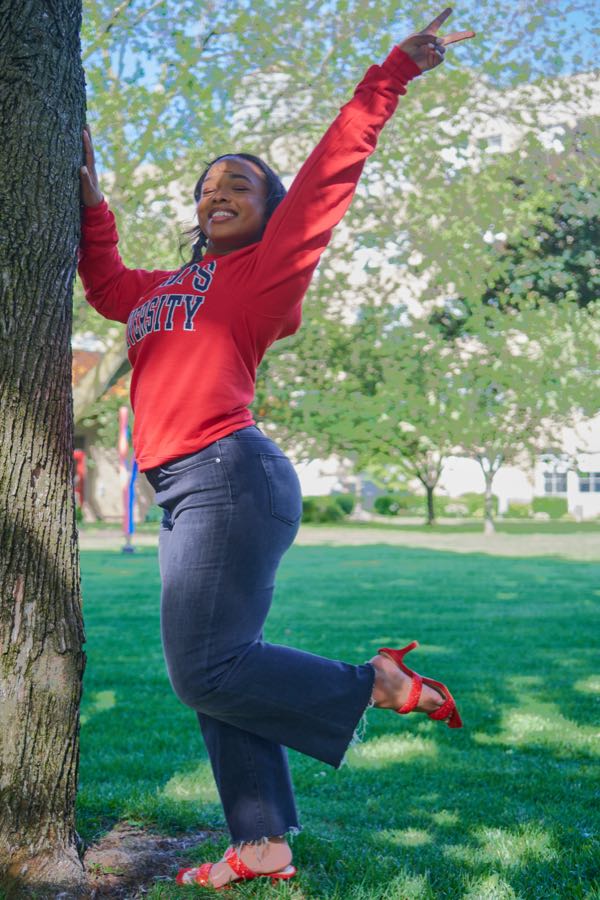 Leaning off a tree on the lawn, arm up, laughing.