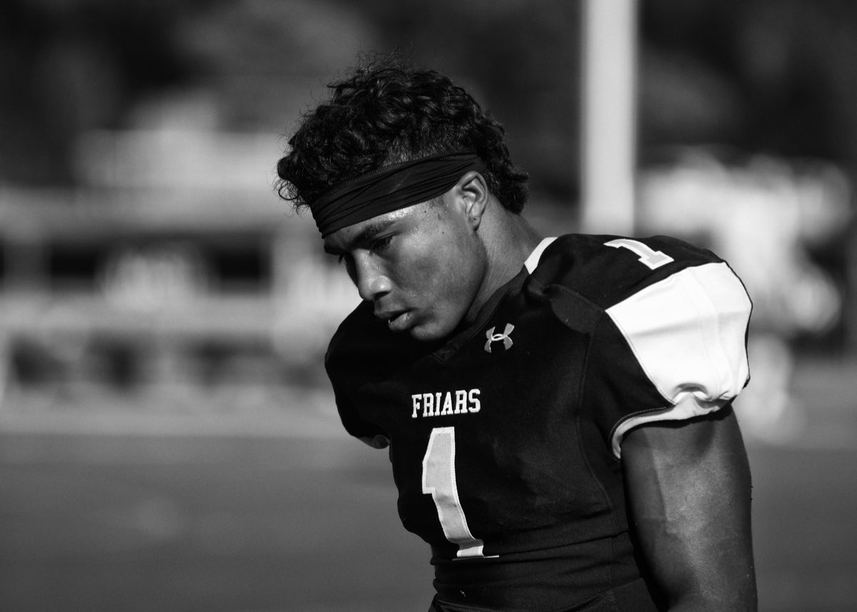 Black and white portrait of a football player in a Friars jersey, head lowered under the lights.
