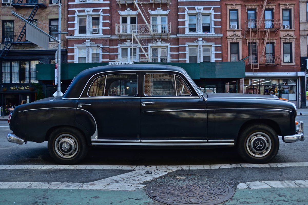 A vintage black Mercedes parked on a New York block in front of brownstones.
