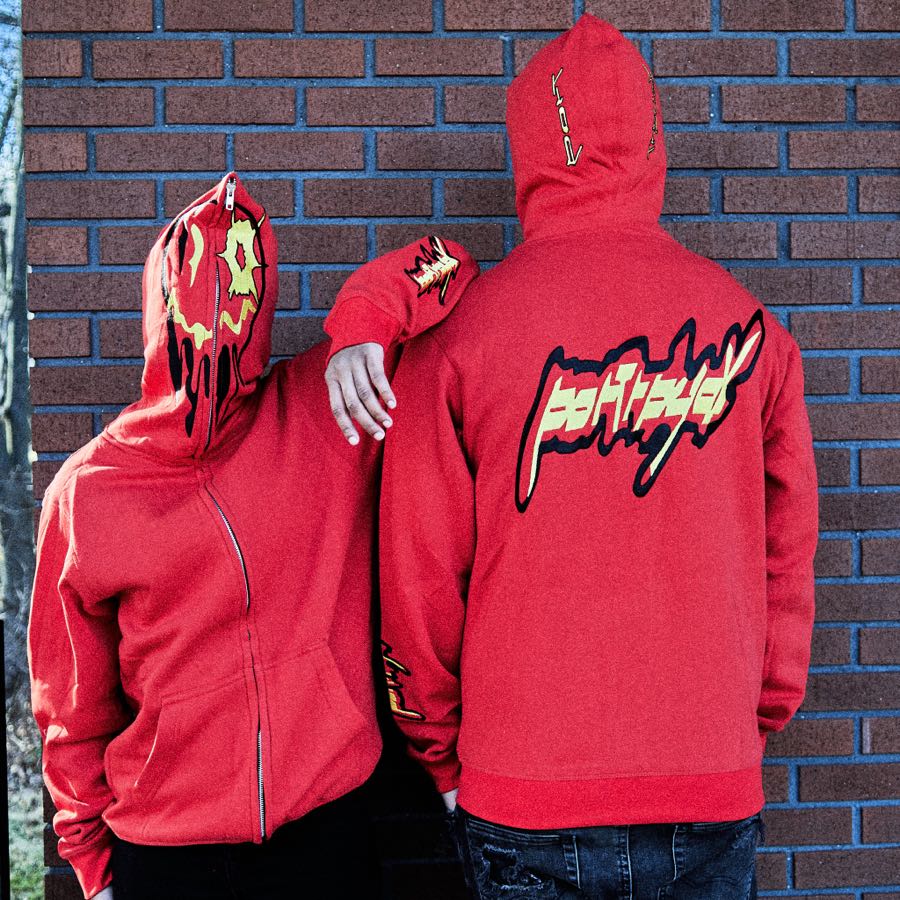 Two models in red Portreyal hoodies leaning against a brick wall, one facing away to show the back print.