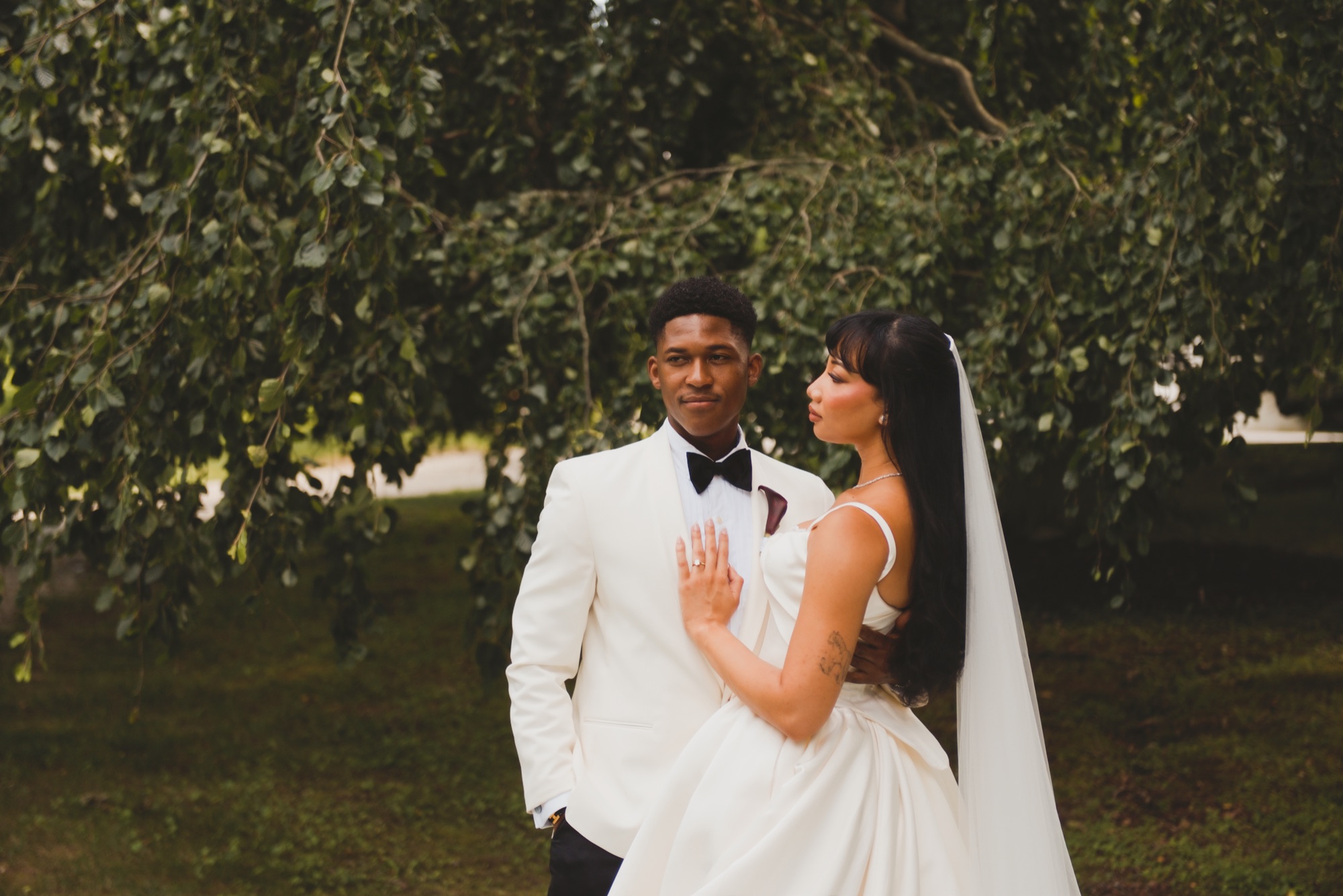 The bride turned toward the groom with her hand on his chest, under hanging branches.